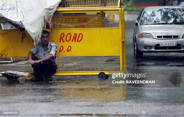 An Indian security guard takes shelter under a covering of jute bags on a barricade during a downpour in New Delhi, 18 June 2007. The Indian capital...