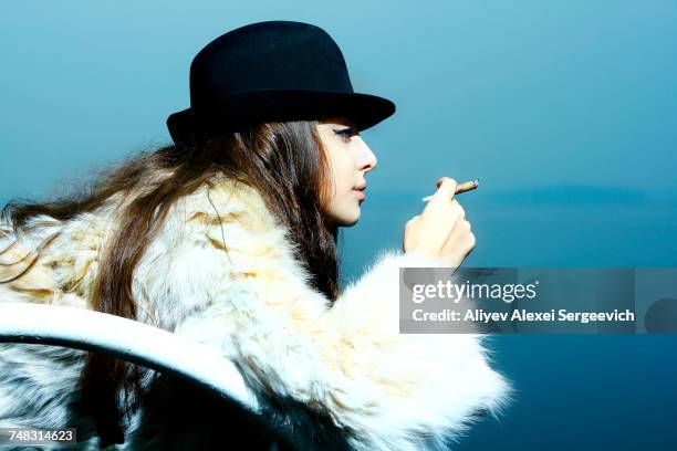 portrait of glamorous woman wearing fur coat smoking cigarette - beautiful women smoking cigars fotografías e imágenes de stock