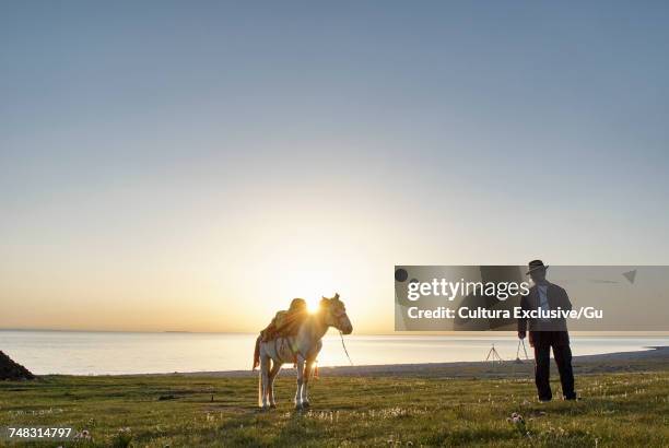 man with horse near beach at sunset, namucuo, xizang, china - cultura china stock-fotos und bilder