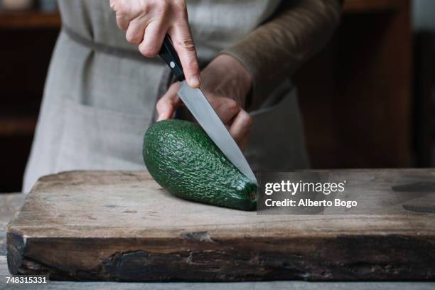 woman slicing avocado on chopping board, mid section - cutting avocado stockfoto's en -beelden