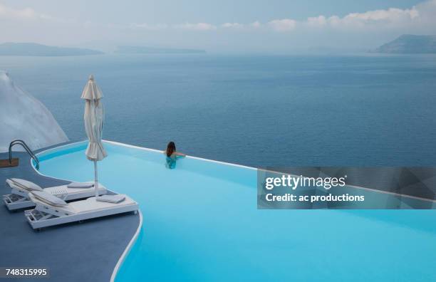 caucasian woman in infinity pool admiring scenic view of ocean - piscine à débordement photos et images de collection