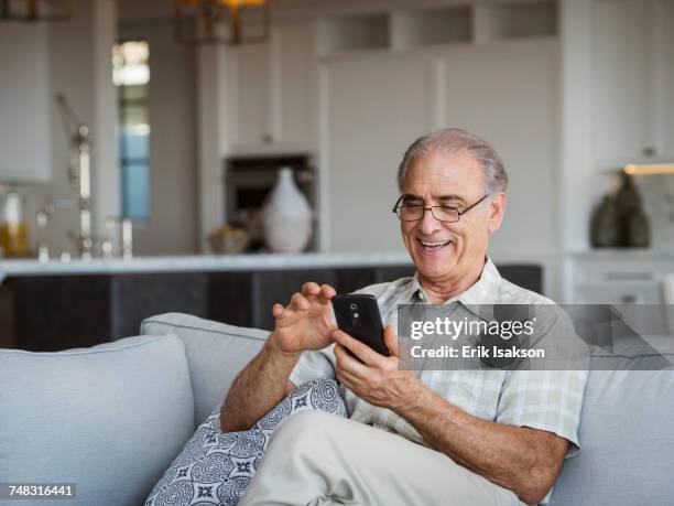 caucasian man sitting on sofa texting on cell phone - old man fotografías e imágenes de stock