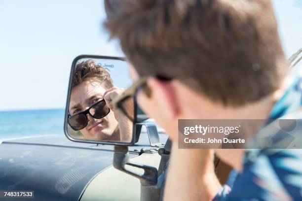 reflection of caucasian man in side-view mirror of car on beach - fahrzeugspiegel stock-fotos und bilder