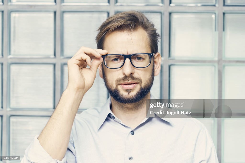 Portrait of businessman holding eyeglasses by office glass wall