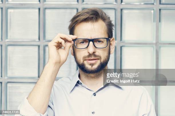 portrait of businessman holding eyeglasses by office glass wall - confusion stock-fotos und bilder