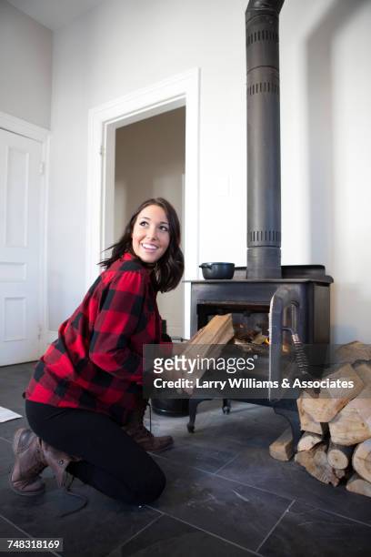 caucasian woman placing wood into stove - brandhout stockfoto's en -beelden