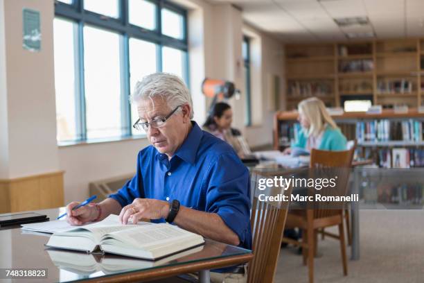 older man reading book in library and writing notes - adult learning stock pictures, royalty-free photos & images