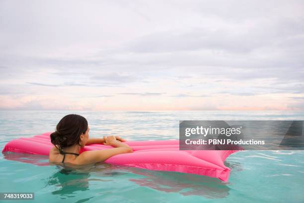 mixed race woman floating in ocean on inflatable raft - warm roze stockfoto's en -beelden