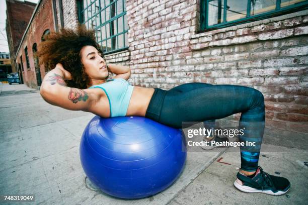 hispanic woman balancing on fitness ball near brick wall - yoga ball outside stock pictures, royalty-free photos & images