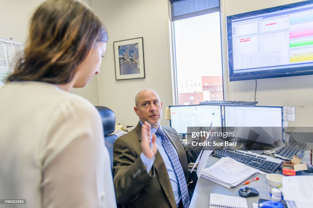 Over shoulder view of manager having discussion with office worker at office desk