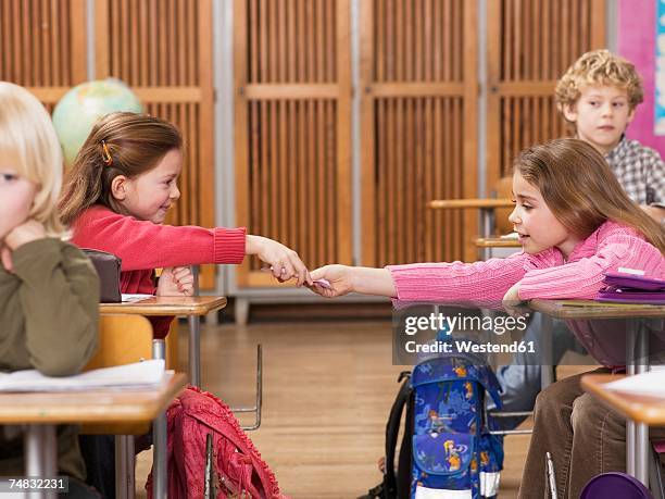 girls (4-7) exchanging notes in classroom - satchel bag stock-fotos und bilder