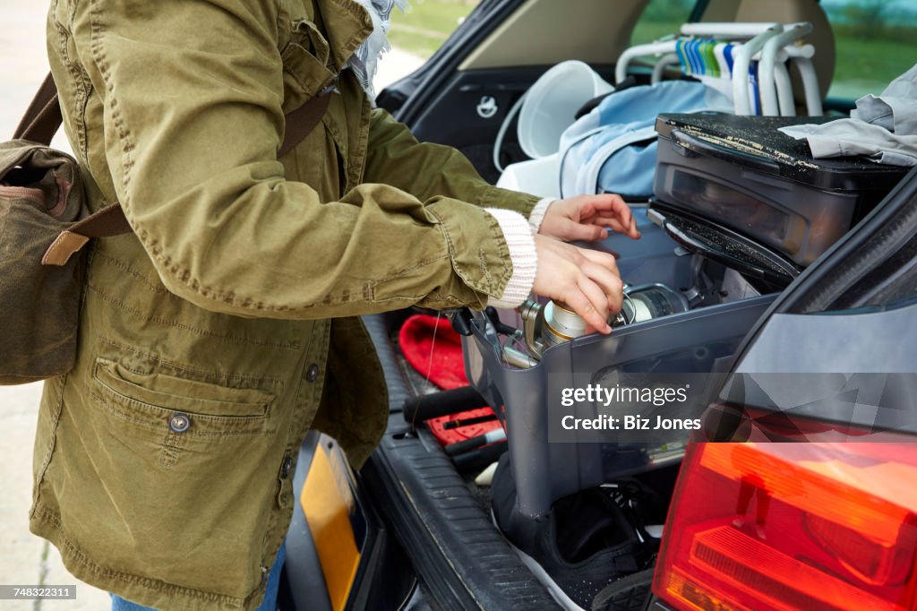 Young woman removing belongings from boot of car, mid section