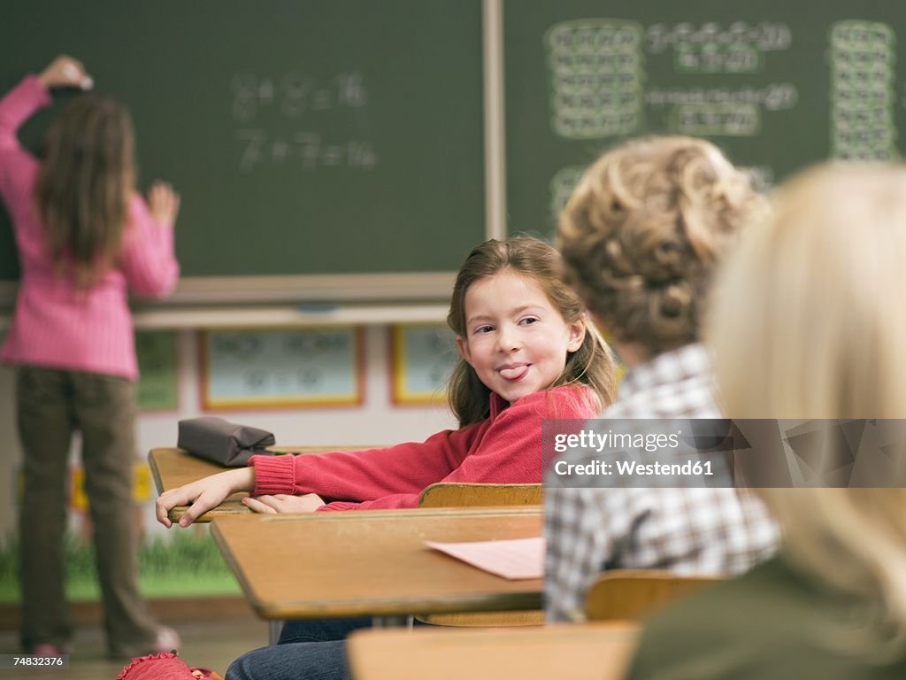 Children (4-7) in class room, focus on girl sticking out tongue