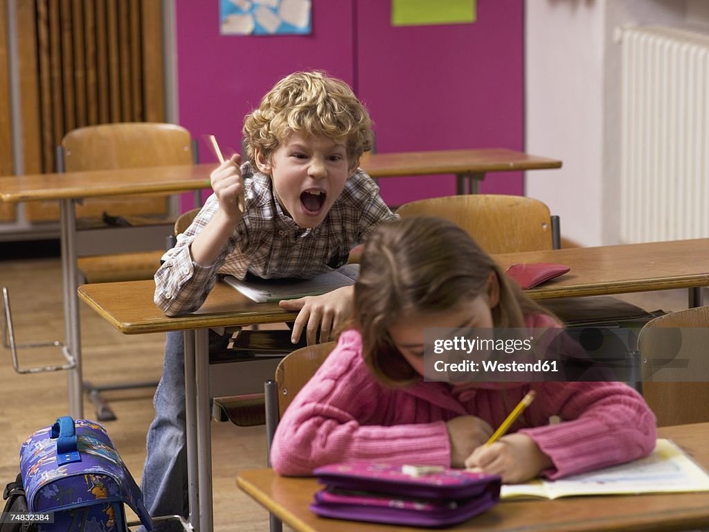 Boy (4-7) shouting behind girl in class room