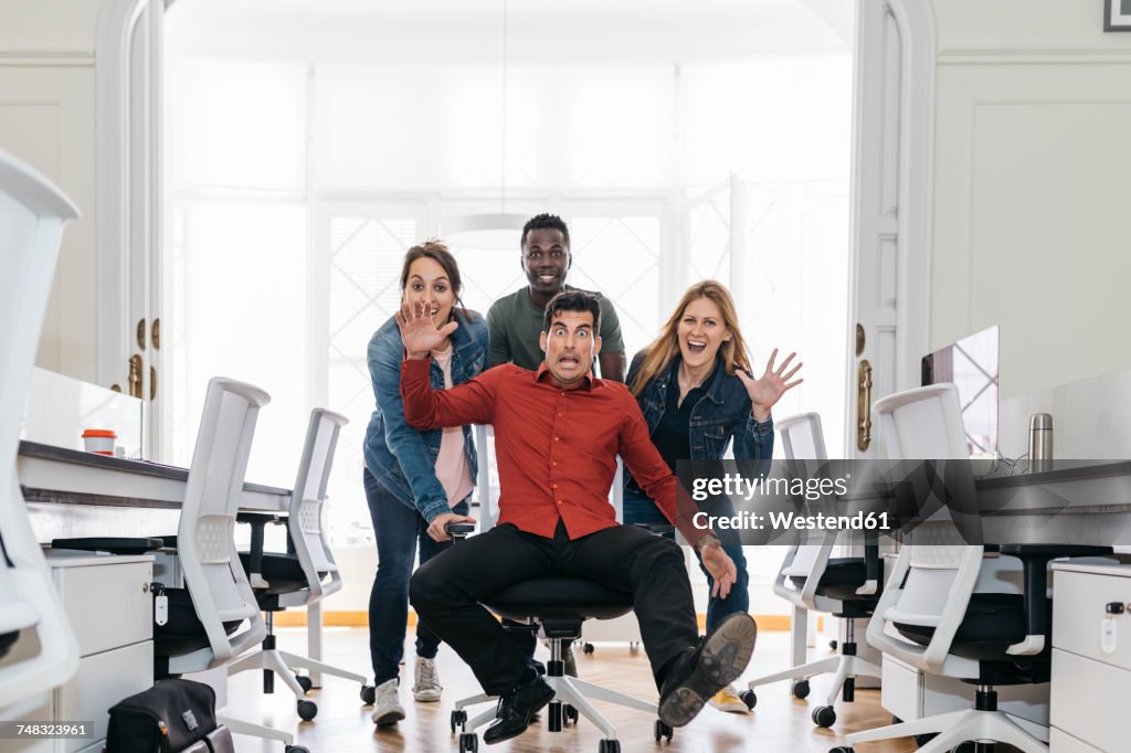 Employees pushing their boss on a swivel chair through the office