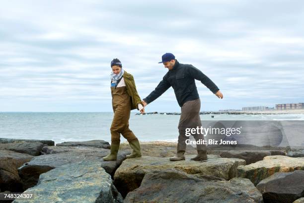 young sea fishing couple stepping over beach rocks - nassau county bildbanksfoton och bilder