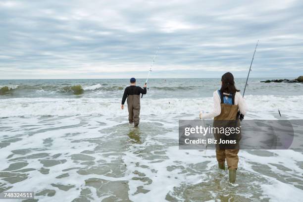 young sea fishing couple in waders, wading in sea - waders stock-fotos und bilder