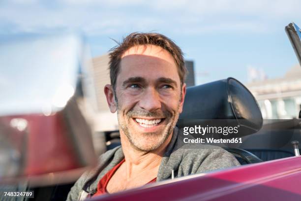 portrait of smiling mature man sitting in his sports car - cabrio stock-fotos und bilder