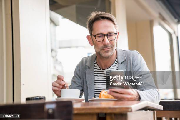 portrait of mature man sitting at sidewalk cafe looking at cell phone - man in cafe stock pictures, royalty-free photos & images