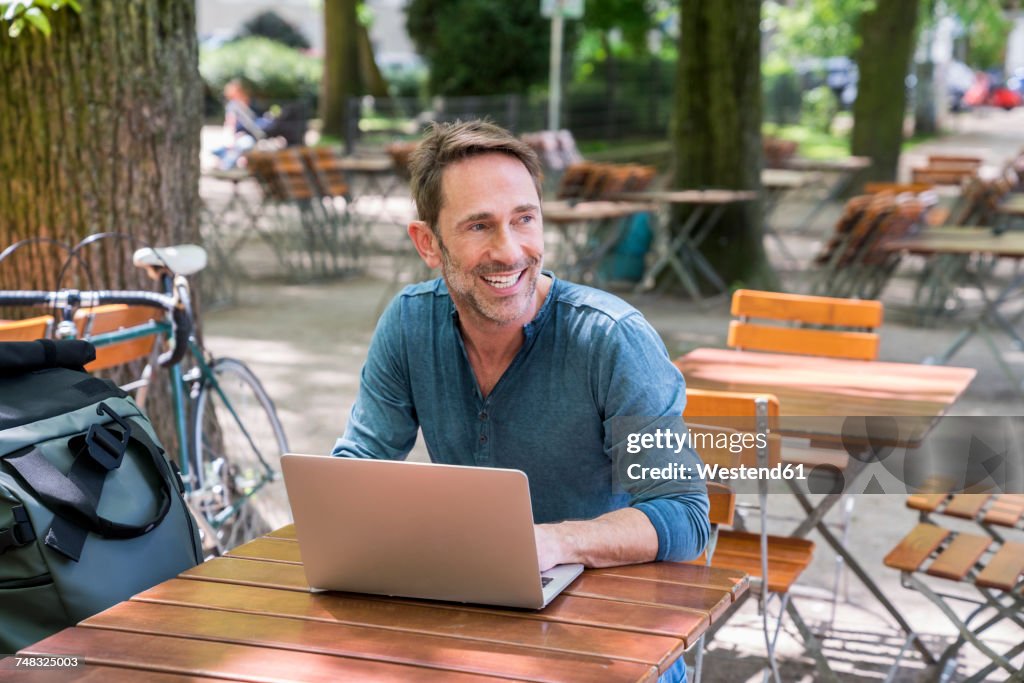 Portrait of smiling mature man using laptop in beer garden