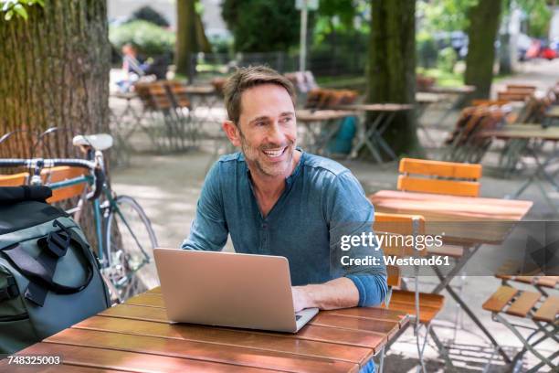 portrait of smiling mature man using laptop in beer garden - biergarten stock-fotos und bilder