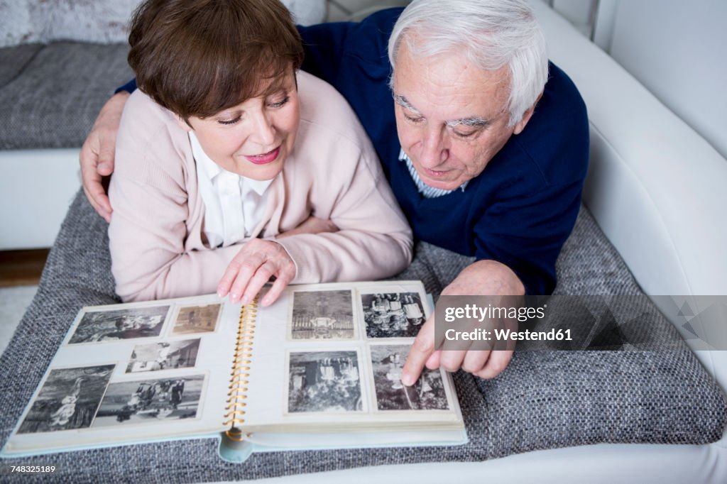 Senior couple lying on couch, looking at photo album