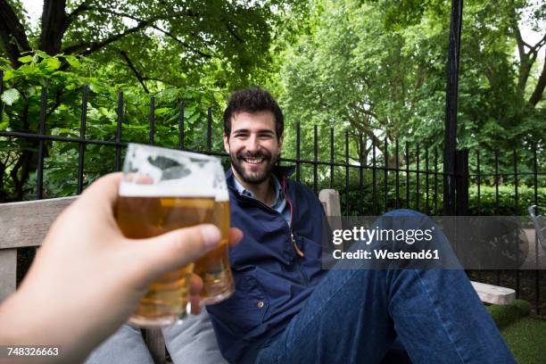 portrait of smiling young man toasting with glass of beer in garden - biergarten stock-fotos und bilder