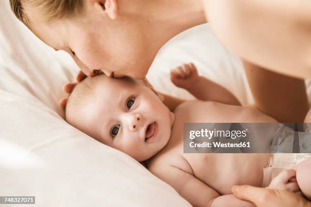 mother kissing her baby lying in bed - attrezzatura per neonato foto e immagini stock