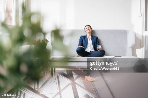 smiling businesswoman sitting on couch with beverage - office sofa stock-fotos und bilder