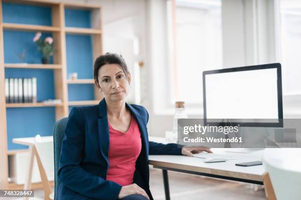 portrait of serious businesswoman sitting at desk in a loft - une seule femme d'âge mûr photos et images de collection