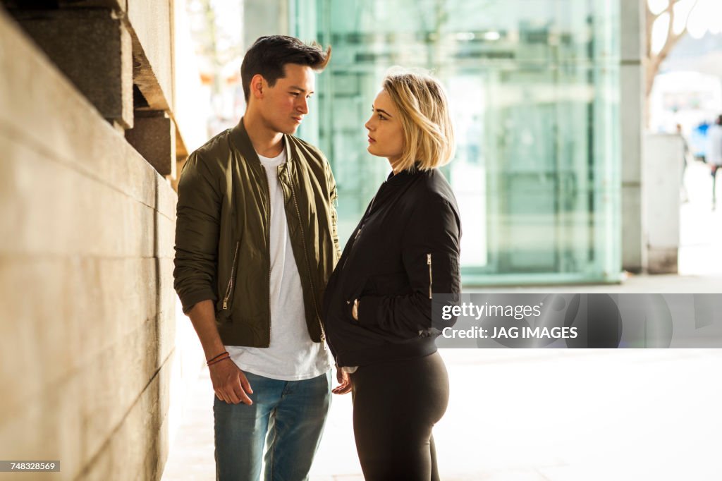 Young couple, outdoors, standing face to face, pensive expressions