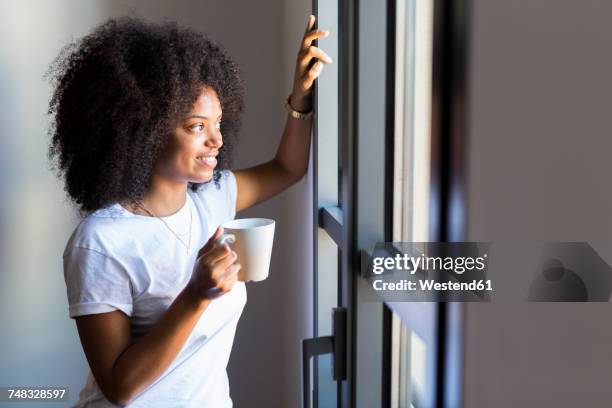 smiling woman holding cup of coffee looking out of window - coffee cup top view stock pictures, royalty-free photos & images