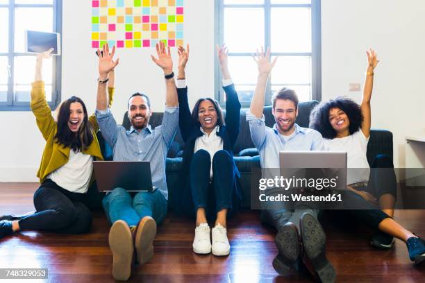 portrait of happy colleagues cheering sitting on floor with laptops - day 5 stockfoto's en -beelden