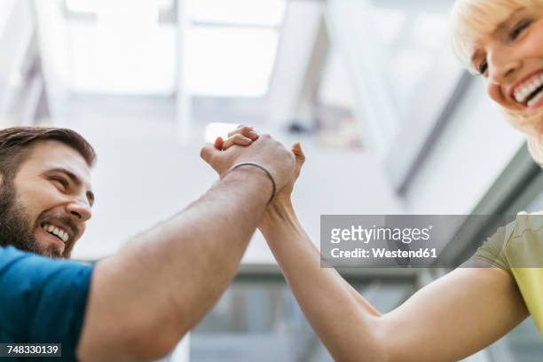 colleagues arm wrestling in office, laughing and having fun - arm wrestle stock pictures, royalty-free photos & images