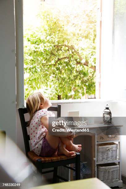 little girl sitting on chair looking out of window - girl side view stock-fotos und bilder
