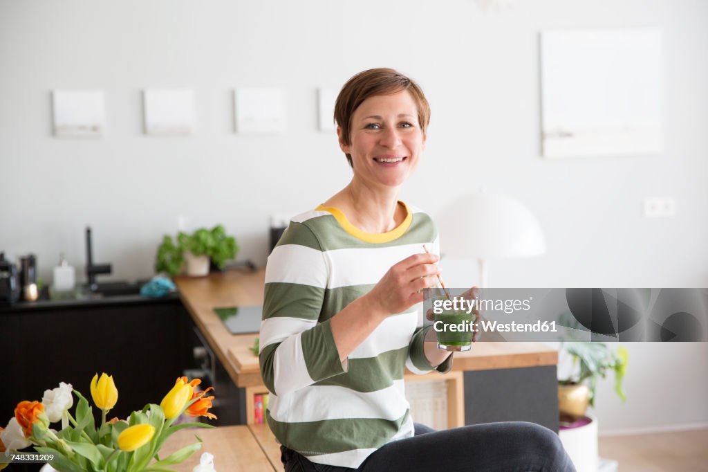 Portrait of smiling woman with green smoothie in the kitchen