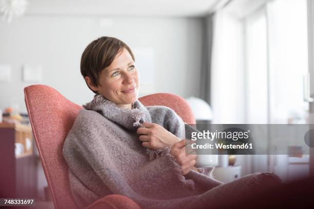 portrait of smiling woman relaxing with cup of coffee at home - wrapped in a blanket stockfoto's en -beelden