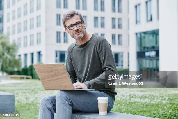mature man outdoors with laptop and takeaway coffee - green economy stock-fotos und bilder
