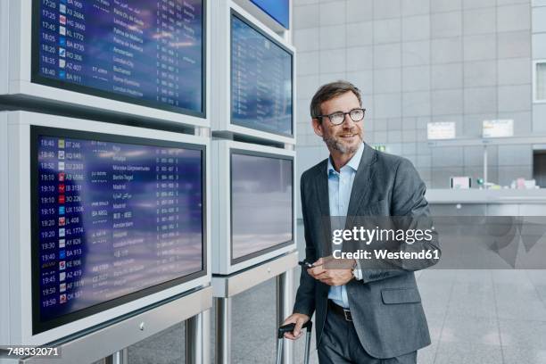 businessman with cell phone at timetable at the airport - abflugbereich stock-fotos und bilder