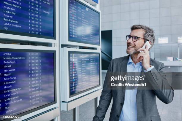 businessman with cell phone at timetable at the airport - airport phone stock-fotos und bilder