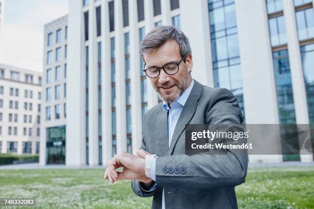 mature businessman outdoors checking his smartwatch - bien vestido fotografías e imágenes de stock