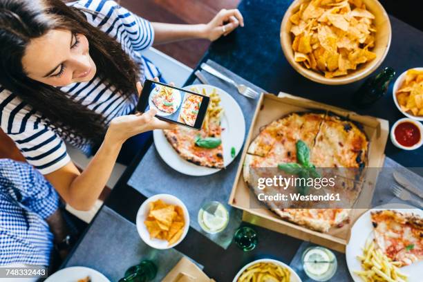 woman taking cell phone picture of pizza on table - woman eating pizza stock-fotos und bilder