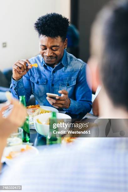 smiling man looking at cell phone at dining table - foodie stock-fotos und bilder