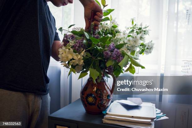 mid section of young man arranging vase of flowers in front of window - arranging flowers foto e immagini stock