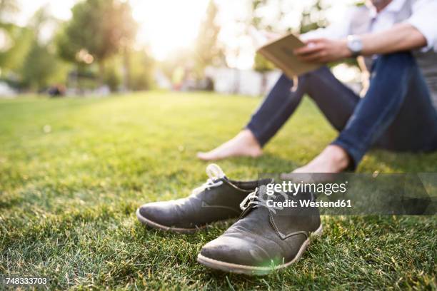 unrecognizable businessman in the city park sitting on grass reading book - mens bare feet stock pictures, royalty-free photos & images