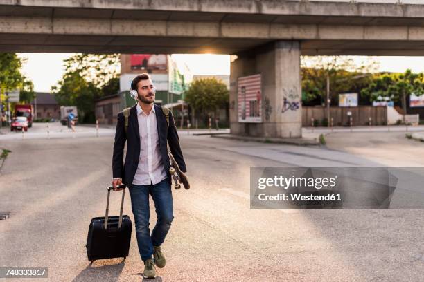 young man on the move with skateboard, rolling suitcase and headphones - music city walk stock pictures, royalty-free photos & images