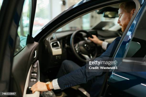 businessman testing car in car dealership - entrando fotografías e imágenes de stock
