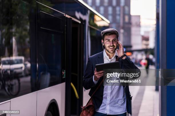 young man at the bus stop in the city with earphones and tablet - bus front stock pictures, royalty-free photos & images