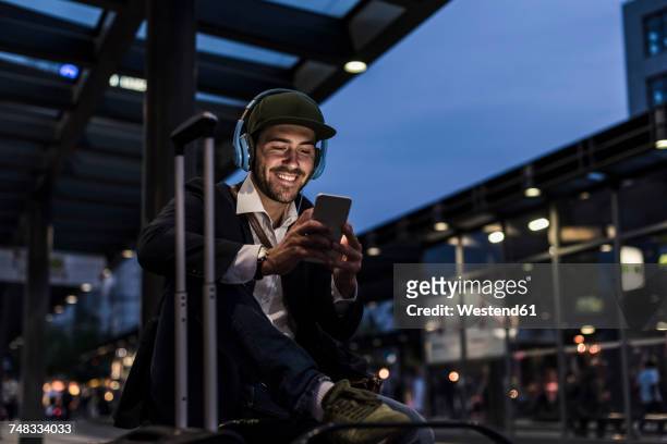 young man in the city with headphones and cell phone in the evening - young man listening to music on smart phone outdoors stockfoto's en -beelden
