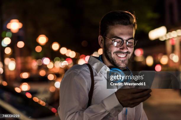 smiling young man in the city checking cell phone at night - lens flare portrait guy stock-fotos und bilder